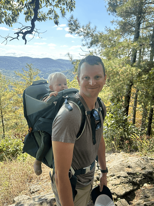 Brian with his son in a hiking backpack on a trail